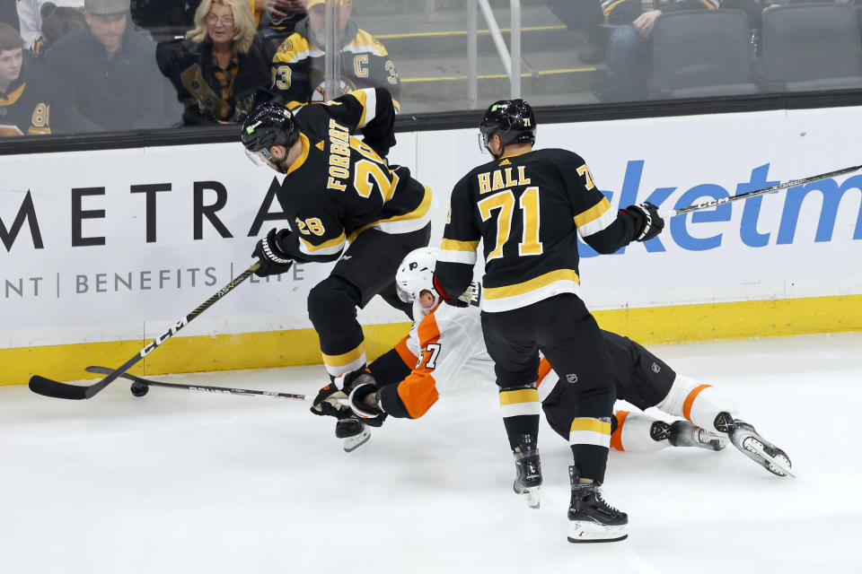 Boston Bruins defenseman Derek Forbort controls the puck ahead of a diving effort from Philadelphia Flyers right wing Wade Allison as Bruins' Taylor Hall (71) looks on during the first period of an NHL hockey game, Monday, Jan. 16, 2023, in Boston. (AP Photo/Mary Schwalm)