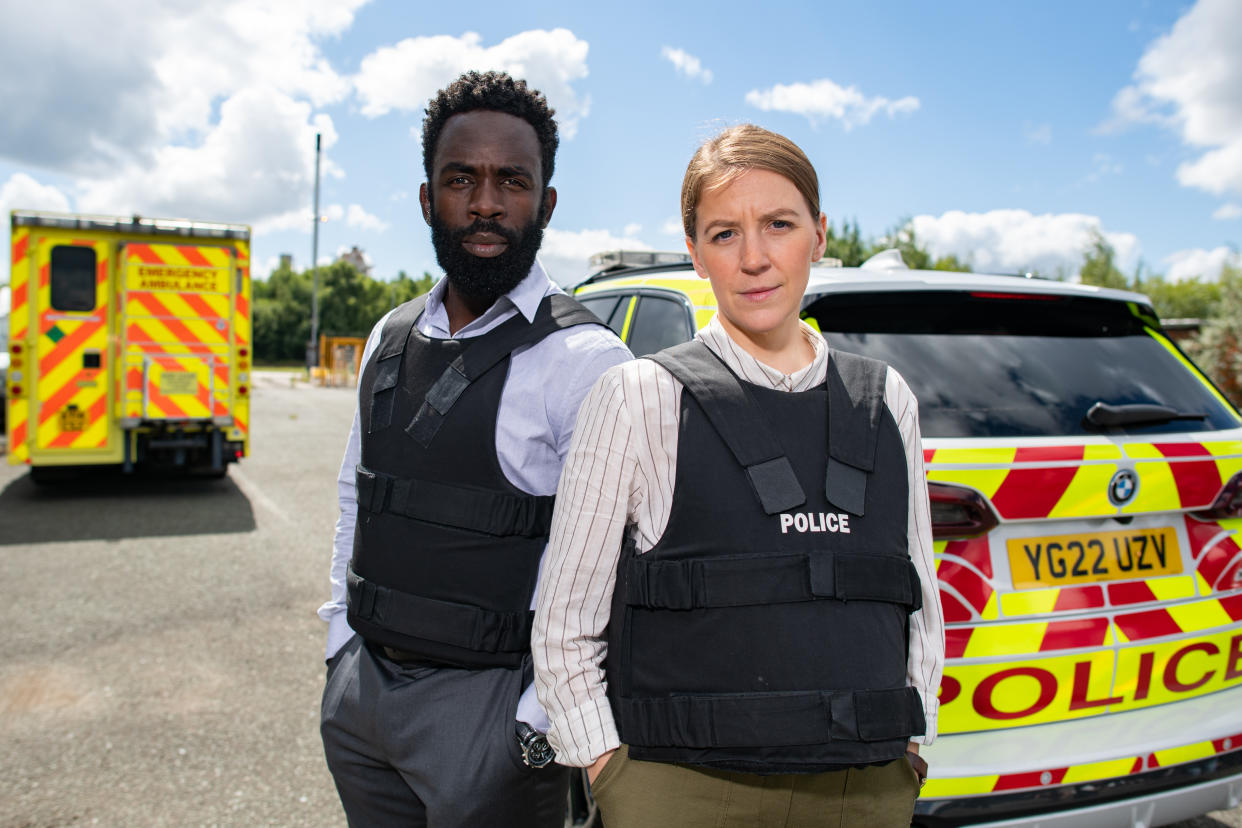  The Tower II: Death Message cast - Gemma Whelan as DS Sarah Collins and Jimmy Akingbola as DC Steve Bradshaw standing in front of a police car. 