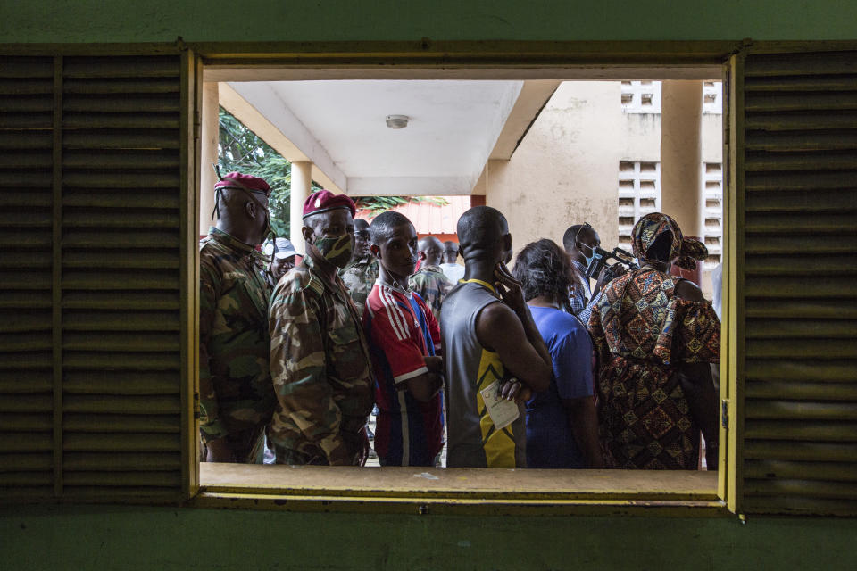 Civilians and soldiers line up to vote at a school in Conakry, Guinea, Sunday Oct. 18, 2020. Guineans head to the polls to elect their president, choosing between incumbent Alpha Conde who is seeking a third term and historical opponent Cellou Dalein Diallo. (AP Photo/Sadak Souici)