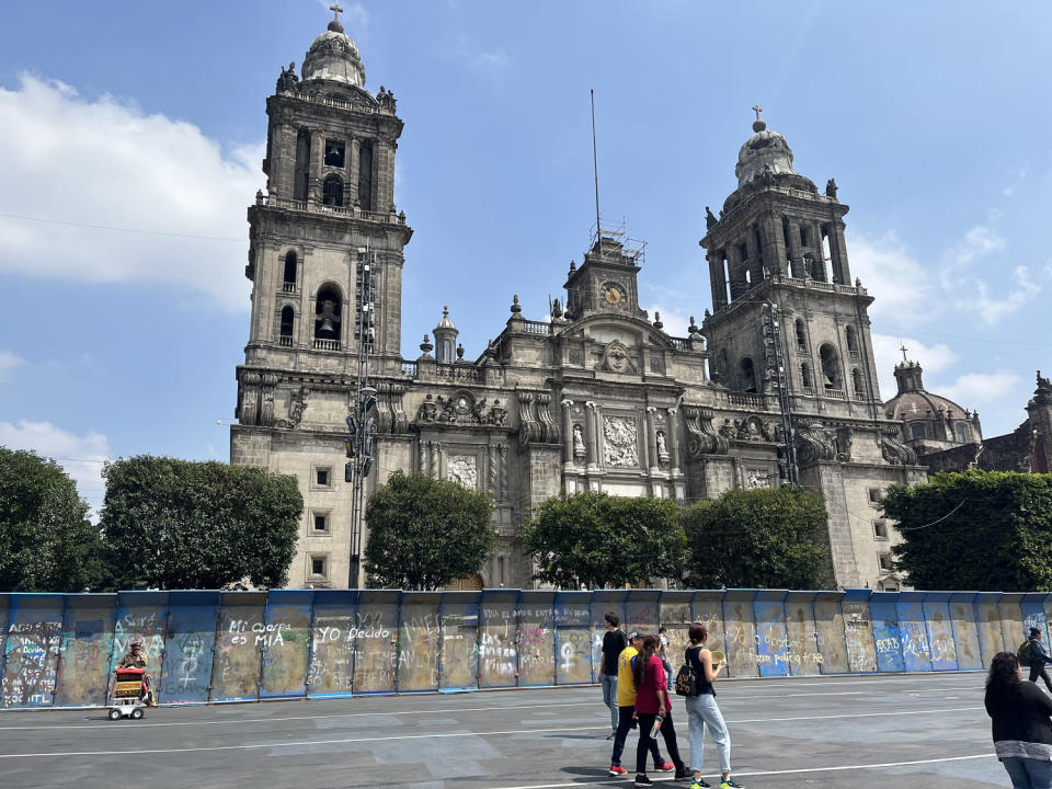 People walk past a metal wall covered in graffiti, blocking the Metropolitan Cathedral (Isabela Espadas Barros Leal / NBC News)