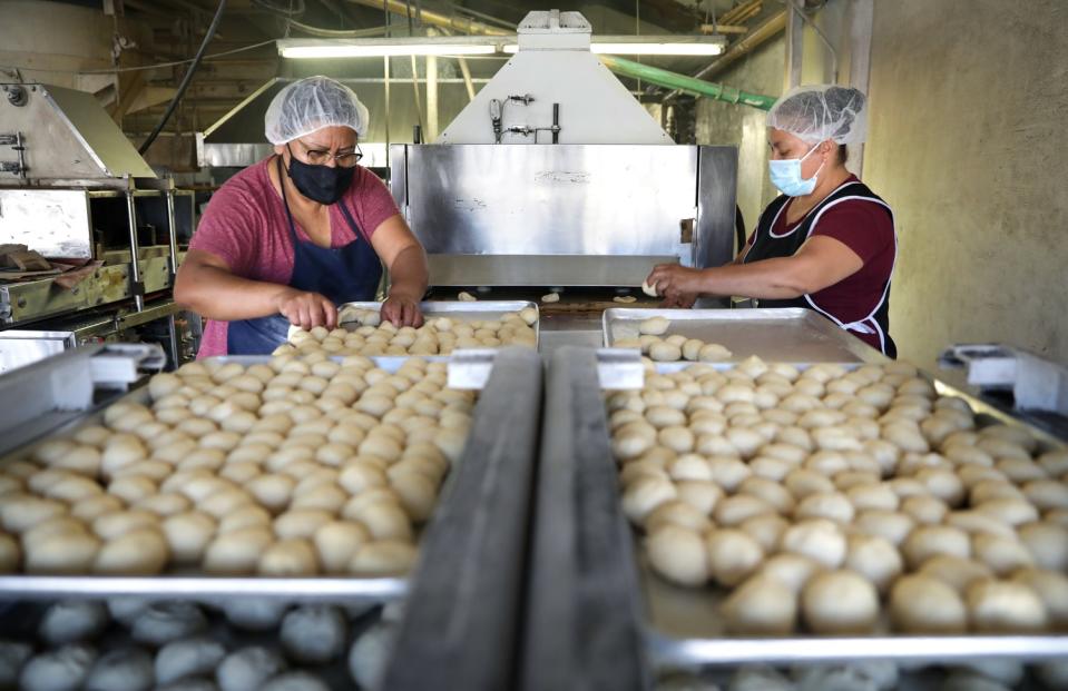 Two workers stand next to balls of dough on a machine