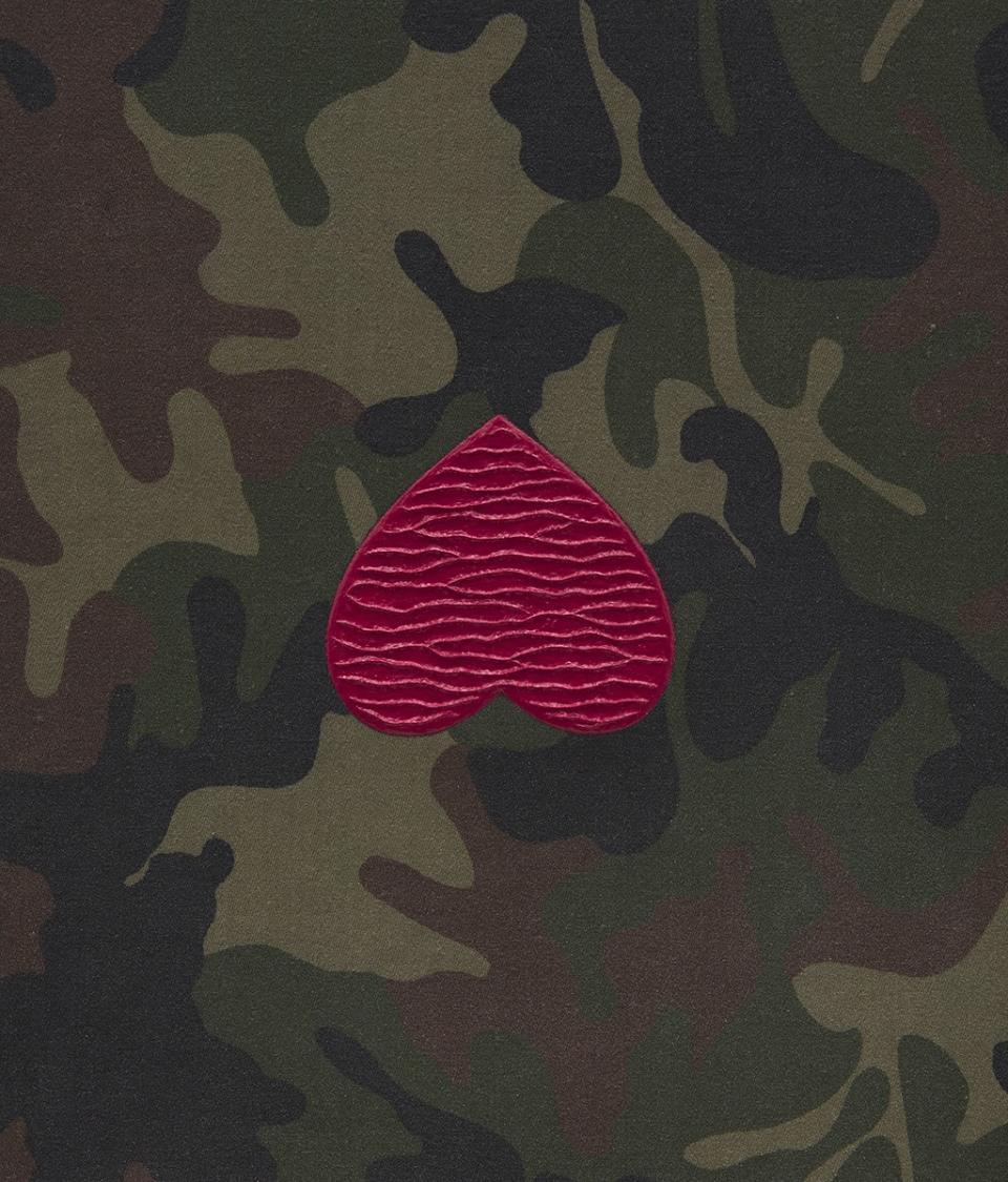 A painting on camouflage in shades of green shows a glittering, upside-down red heart at its middle