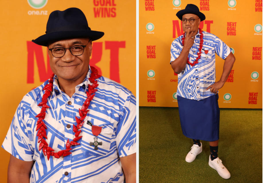 Man in patterned shirt, fedora, lei necklace, and glasses posing with hand gesture on hip