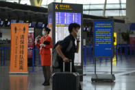 A passenger wearing a face mask to help curb the spread of the coronavirus pushes his luggage past a masked airliner staff stand near quiet check-in counters at Pudong International Airport in Shanghai, China, Sunday, July 25, 2021. Airline flights were canceled in eastern China and cargo ships were ordered out of the area Saturday as Typhoon In-fa churned toward the mainland after dumping rain on Taiwan. (AP Photo/Andy Wong)