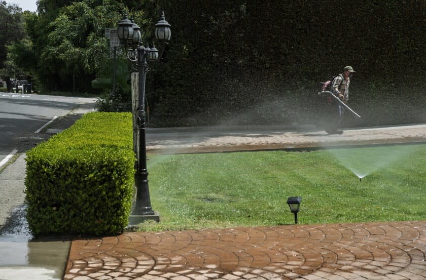 LOS ANGELES, CA-APRIL 28, 2022: A gardener uses a leaf blower while cleaning a driveway as sprinklers water the front lawn of a home on Sunset Blvd. near Carmelina Ave. in Los Angeles. (Mel Melcon / Los Angeles Times)