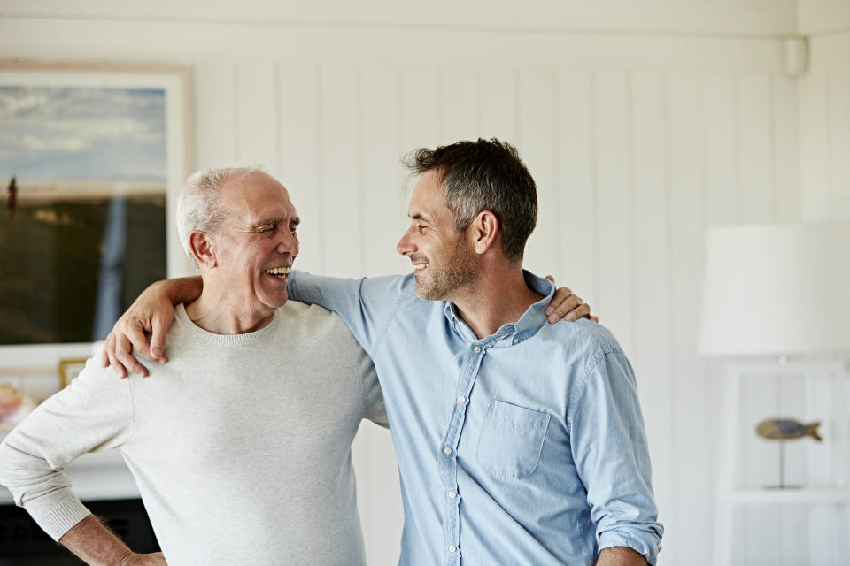 Father and son, one older and one middle-aged, smiling and embracing in a loving and friendly gesture