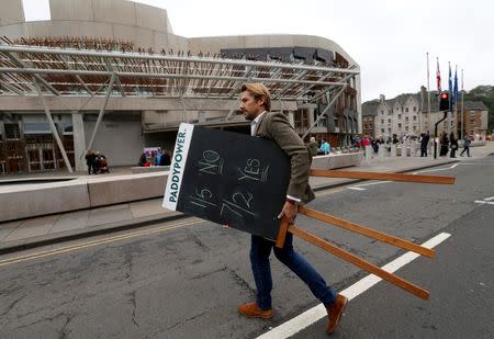 A bookmaker carries a blackboard with odds chalked onto it, outside the Scottish Parliament in Edinburgh, in Scotland September 17, 2014. REUTERS/Russell Cheyne