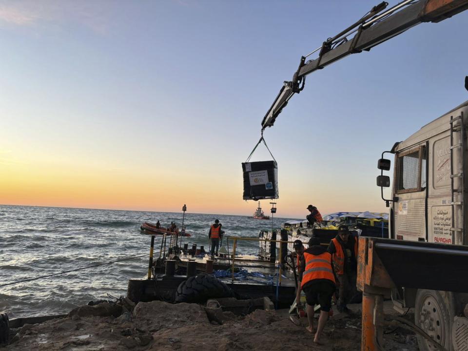 This photo provided by World Central Kitchen shows a crane unloading food packages over a makeshift port on the Gaza Strip, Saturday, March 16, 2024. Spanish NGO Open Arms has sent essential aid to Gaza by a barge towed by a ship from Cyprus. The food was sent by World Central Kitchen, the charity founded by celebrity chef José Andrés, which operates kitchens providing free meals in Gaza. WCK said that it was offloading almost 200 tons of rice, flour and proteins on Saturday and that a second vessel is preparing to set sail from Cyprus with hundreds more tons of food. (World Central Kitchen via AP)