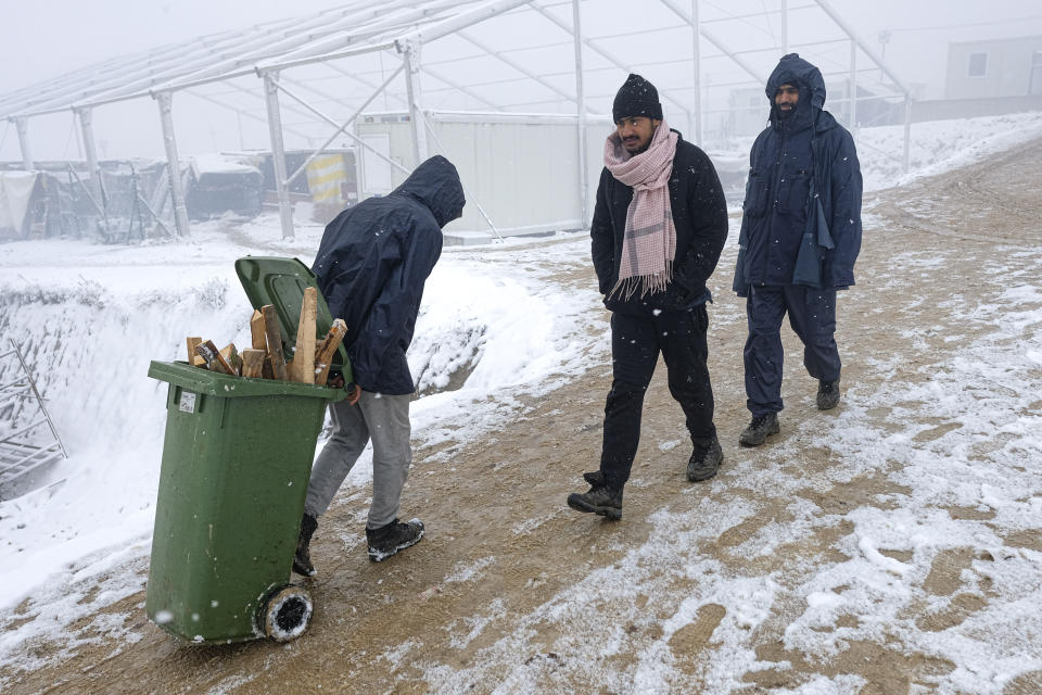A migrant carries firewood in garbage container at the Lipa camp, outside Bihac, Bosnia, Friday, Jan. 8, 2021. A fresh spate of snowy and very cold winter weather on has brought more misery for hundreds of migrants who have been stuck for days in a burnt out camp in northwest Bosnia waiting for heating and other facilities. (AP Photo/Kemal Softic)