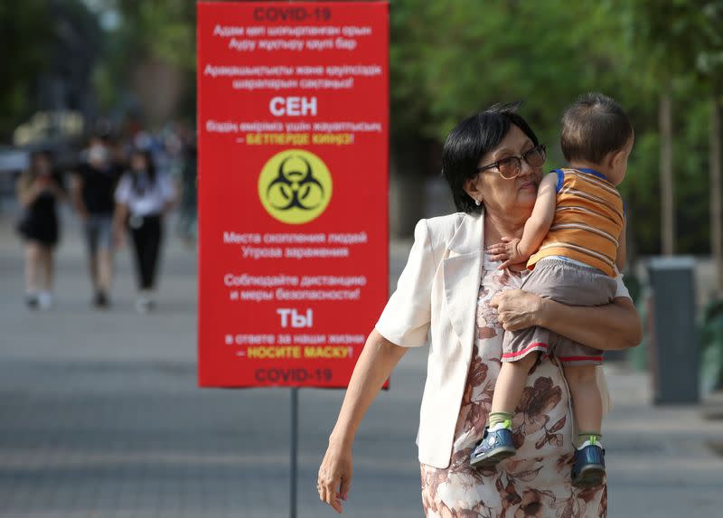 People walk past a board informing of preventive measures against the coronavirus disease in Almaty