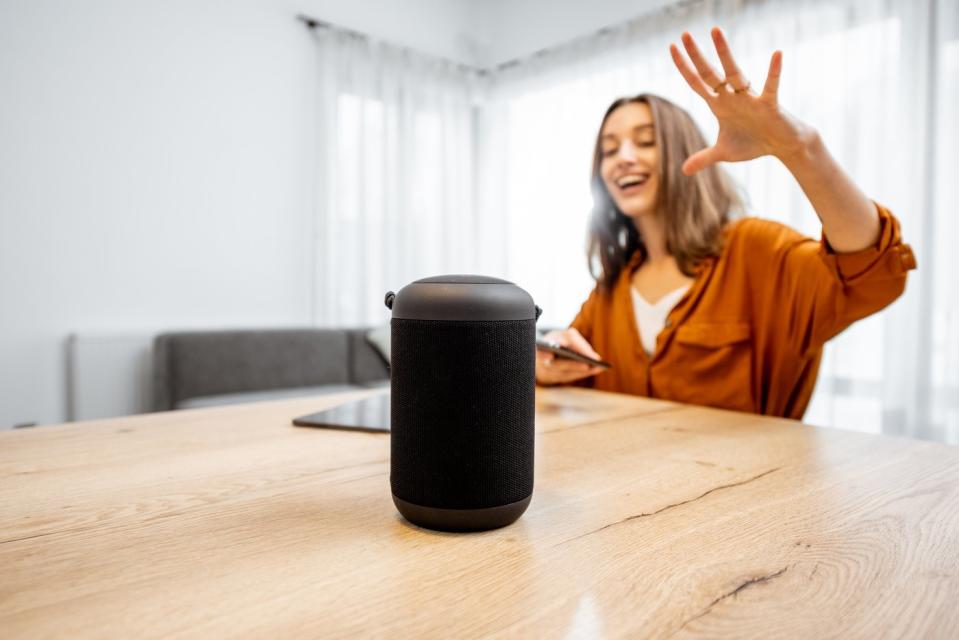 Smiling person interacts with a voice assistant device.