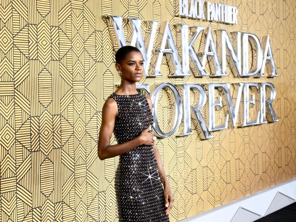 Letitia Wright in black crystal dress in front of gold Wakanda Forever sign