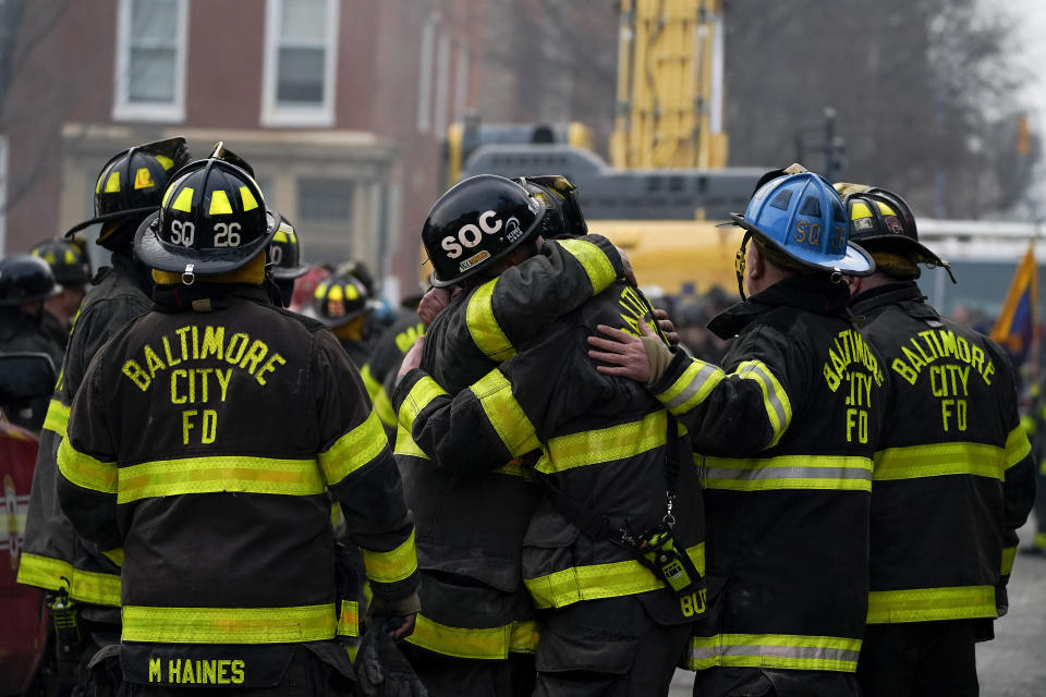 Firefighters embrace each other after a deceased firefighter was pulled out of a building collapse while battling a two-alarm fire in a vacant row home, Monday, Jan. 24, 2022, in Baltimore. Officials said several firefighters died during the blaze. (AP Photo/Julio Cortez)