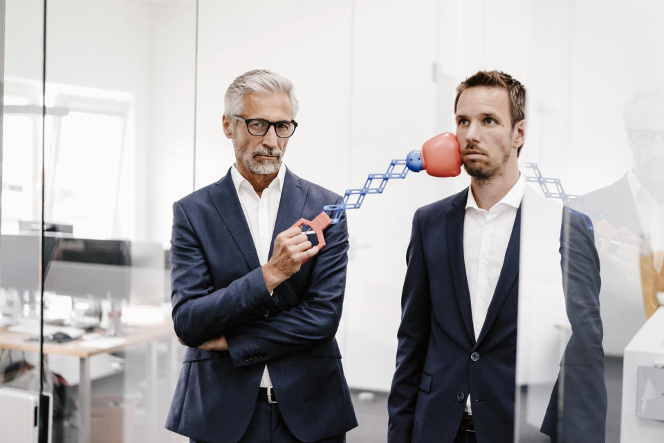 Mature businessman in office hitting colleague with boxing toy