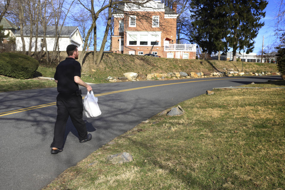 Restaurant owner Joshua Berkowitz makes a food delivery as he walks inside what's called a "containment area" in New Rochelle, N.Y., Wednesday, March 11, 2020. Berkowitz, owner of the Eden Wok restaurant inside the containment area, said customers have been grateful for deliveries. Many felt, he said, as though New Rochelle is under a black cloud - and he sees part of his goal to make them feel like human beings. (AP Photo/Chris Erhmann)