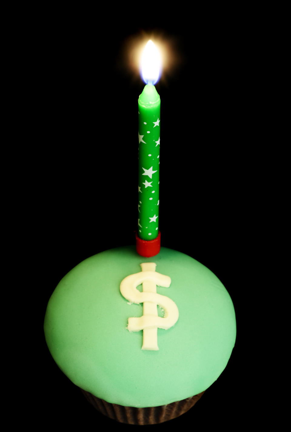 lit candle on a cupcake that has a dollar sign written in icing