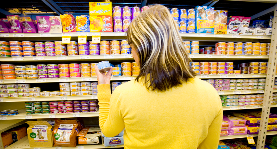 A woman with her back to camera looking at a tin of pet food in the supermarket.