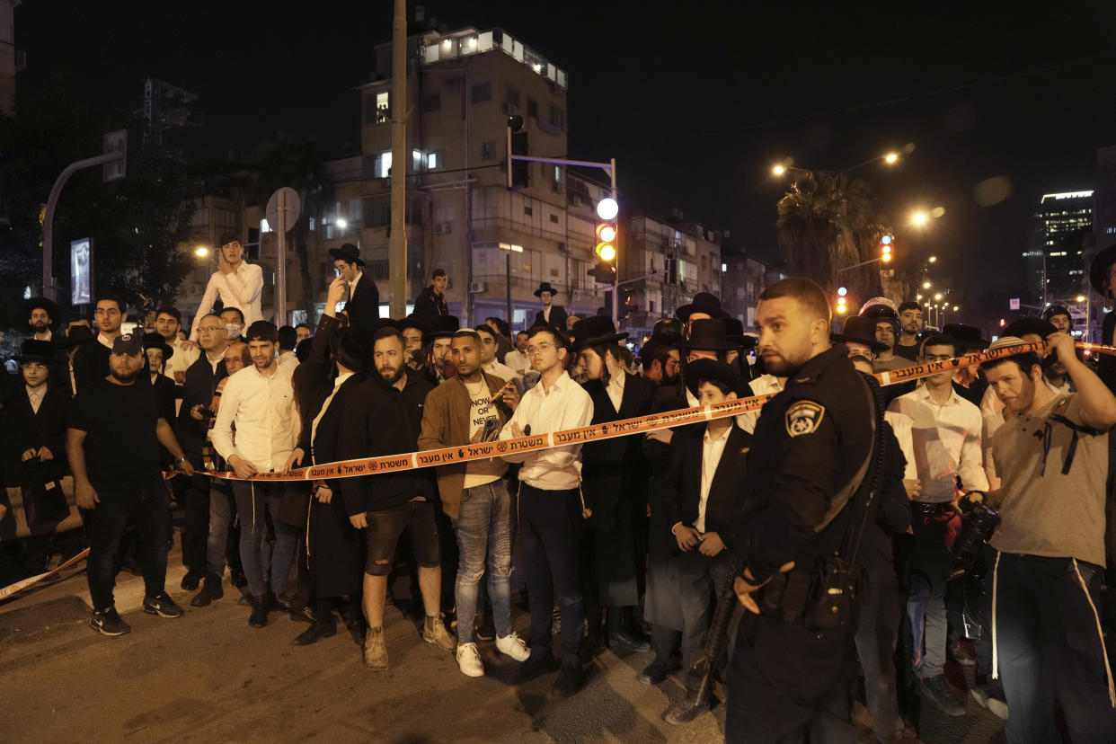 A crowd gathers to watch police working at the site where a a gunman opened fire in Bnei Brak, Israel, Tuesday, March 29, 2022. The circumstance of the deadly incident in the city east of Tel Aviv were not immediately clear. (AP Photo/Oded Balilty)