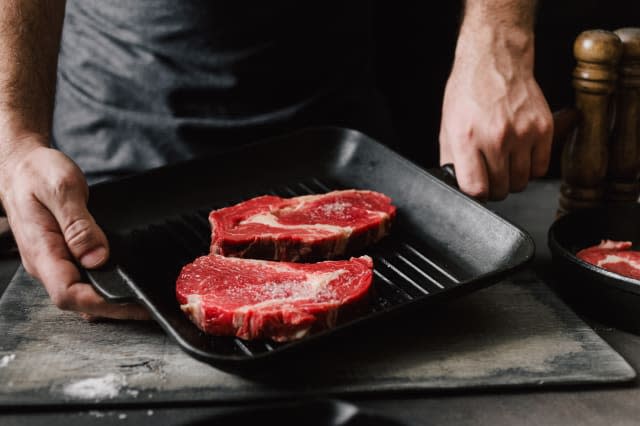 Man cooking beef steaks Male hands holding a grill pan with beef steaks on kitchen