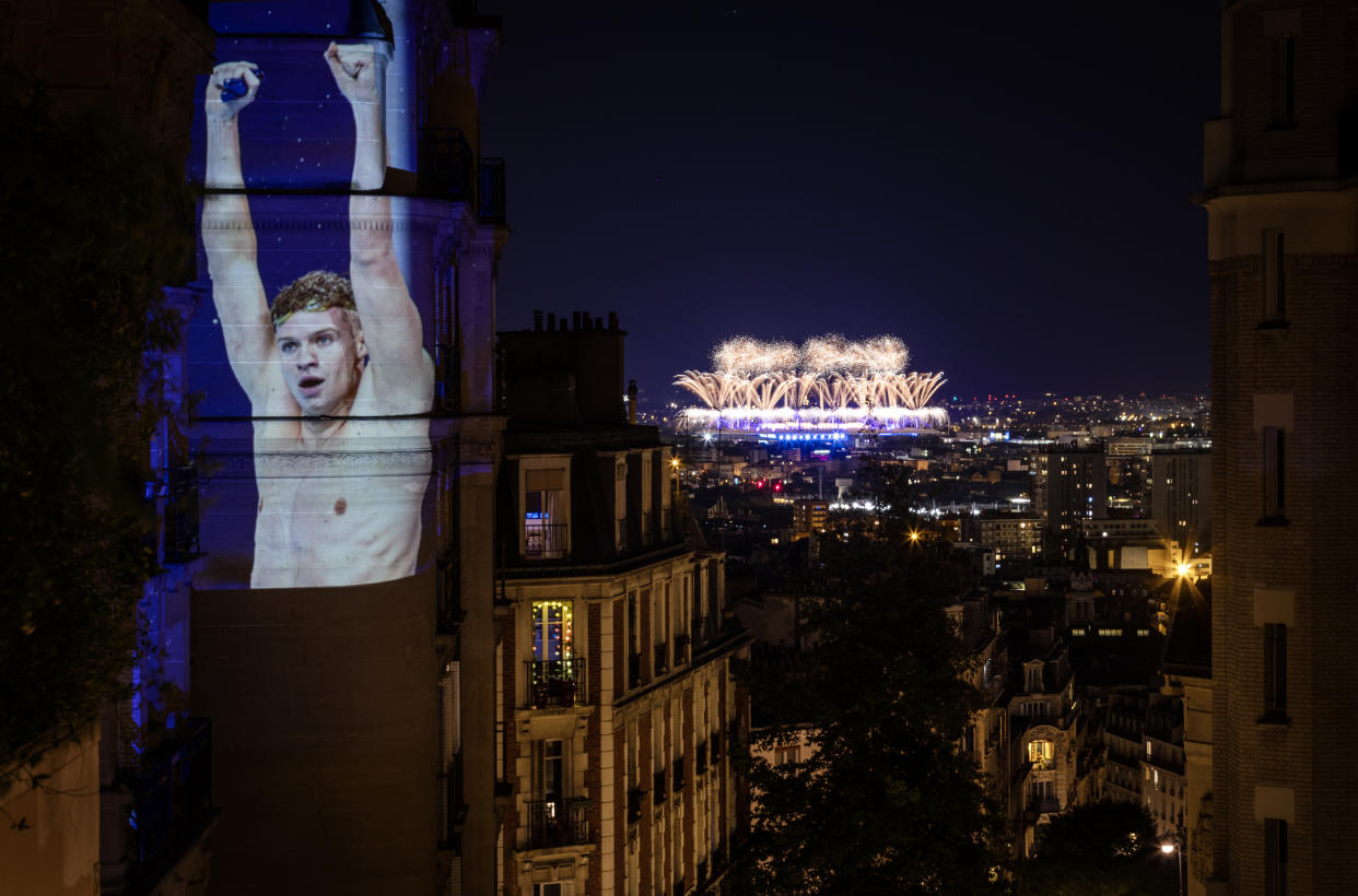 PARIS, FRANCE - AUGUST 11: A photograph of Swimming Gold medalist Leon Marchand of Team France celebrating winning the Men's 200m Individual Medley Final is projected in Montmartre overlooking the fireworks during the Paris 2024 Olympic Games Closing Ceremony at Stade de France as part of Parisienne Projections on August 11, 2024 in Paris, France. Parisienne Projections is a Getty Images project which displays the heroics and tragedies of 16 days of Olympic competition throughout the host city of Paris. Parisienne Projections is a Getty Images project which displays the heroics and tragedies of 16 days of Olympic competition throughout the host city of Paris. (Photo by Ryan Pierse/Getty Images)