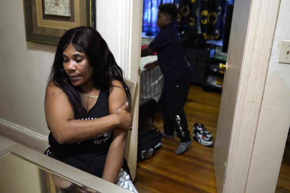 Evena Joseph, of Boston, left, mother of Ryan Mathurin, 9, behind right, is seated at the dining room table as J. Ryan places his book bag in his room after working on his homework at their home, Thursday, Dec. 22, 2022, in Boston. (AP Photo/Steven Senne)