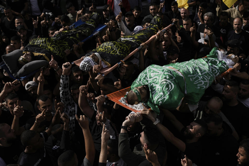 Mourners carry the bodies of three Palestinians draped in the Hamas and Islamic Jihad militant group flags during their funeral in the Jenin refugee camp, West Bank Friday, Nov. 17, 2023. Israeli forces killed the three men in an overnight raid, the Palestinian Health Ministry said Friday. The military wing of the Palestinian Islamic Jihad group claimed the three, including local commander Jamal Lahlouh, 23, as members. (AP Photo/Majdi Mohammed)