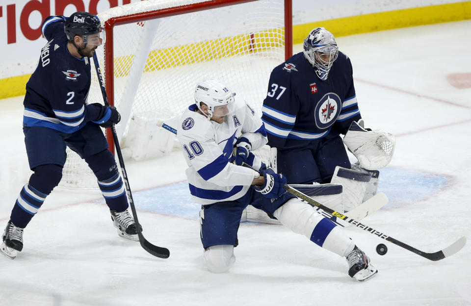 Tampa Bay Lightning's Corey Perry (10) tips the puck toward Winnipeg Jets goaltender Connor Hellebuyck (37) as Jets' Dylan DeMelo (2) defends during second-period NHL hockey game action in Winnipeg, Manitoba, Friday, Jan. 6, 2023. (John Woods/The Canadian Press via AP)