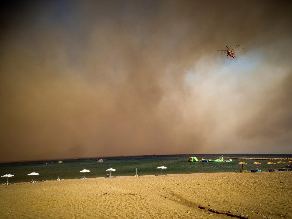 A firefighting helicopter flies over a beach during a forest fire on the island of Rhodes (AP)