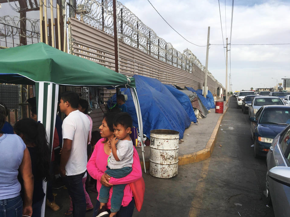 FILE - In this May 5, 2019, file photo, migrants walk between tents, left, and cars waiting to cross the border in San Luis Rio Colorado, Mexico, and Arizona. Newly unsealed court documents show that many U.S. holding cells along the Mexican border were less than half-full, or even empty, during an unprecedented surge of asylum-seeking Central American families. The documents cast doubt on the Trump administration's claims that people had to wait in Mexico because there weren't enough resources to accommodate them. (AP Photo/Elliot Spagat, File)