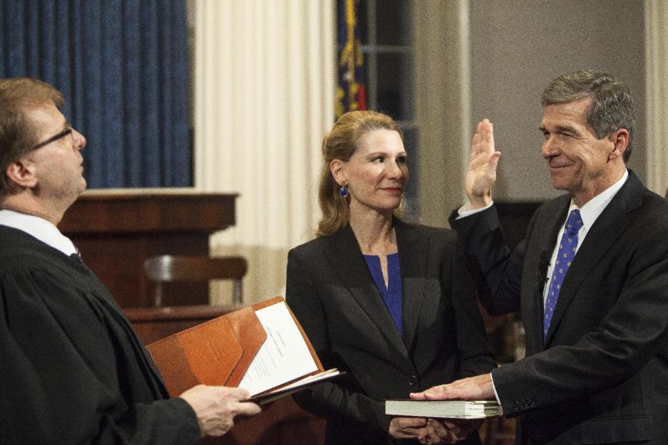 File-In this Jan. 1, 2017 photo Roy Cooper, right, is sworn in as North Carolina governor by North Carolina Supreme Court Justice Mark Martin as Cooper's wife, Kristin, watches in the historic Capitol Building shortly after midnight in Raleigh, N.C. In politically divided North Carolina, weary voters hope top elected officials can put aside differences and effectively govern after a bruising election and a partisan tug-of-war that has spilled into court. (AP Photo/Ben McKeown, Pool)