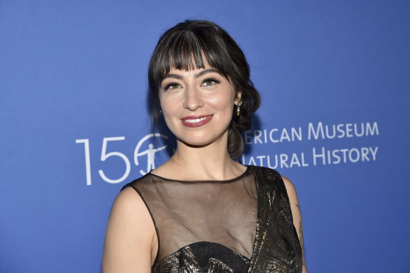 A woman with dark brown hair in an updo smiling against a blue background