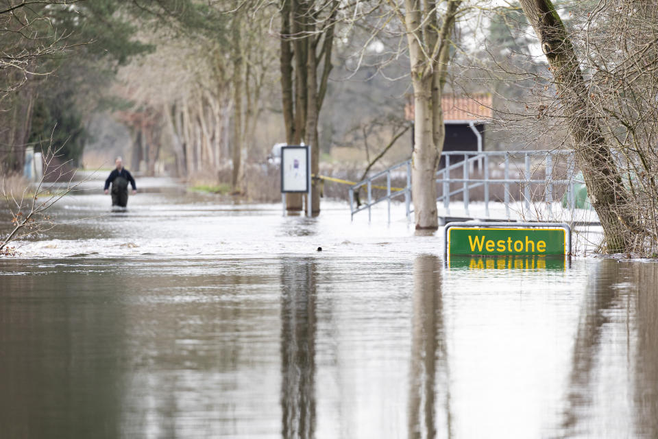 A person walks on a flooded street in the Westohe settlement in the municipality of Winsen (Aller) in the district of Celle, which lies on the River Aller, Germany, Saturday Dec. 30, 2023. On Saturday night, the municipality of Winsen/Aller and the town of Celle were warned of possible power and mobile phone outages due to the expected rise in water levels. (Michael Matthey/dpa via AP)