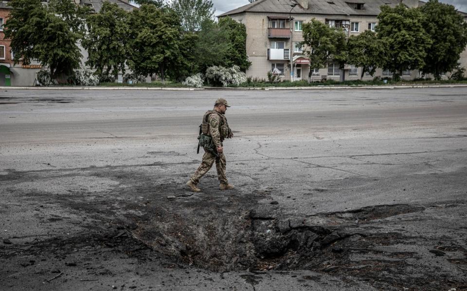 A soldier with the Ukrainian Territorial Defense Forces walks past a crater from a Russian strike in Barvinkove, Ukraine - Finbarr O'Reilly/The New York Times