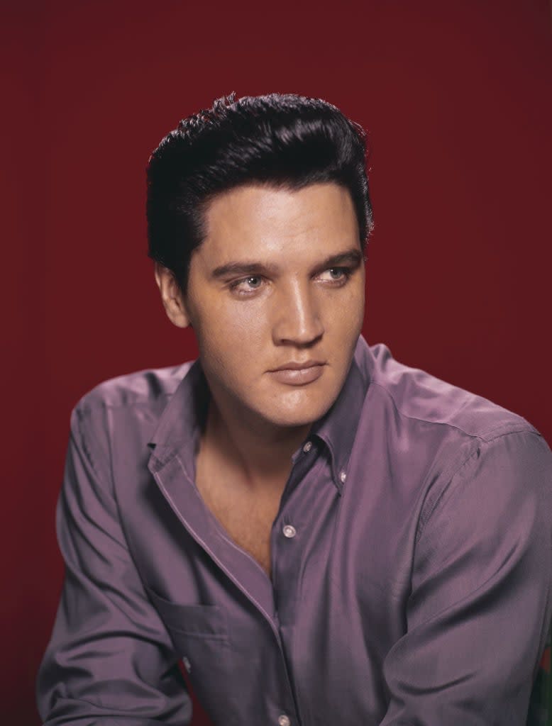 Elvis Presley in a studio portrait, wearing a casual button-up shirt and gazing to the side against a plain background