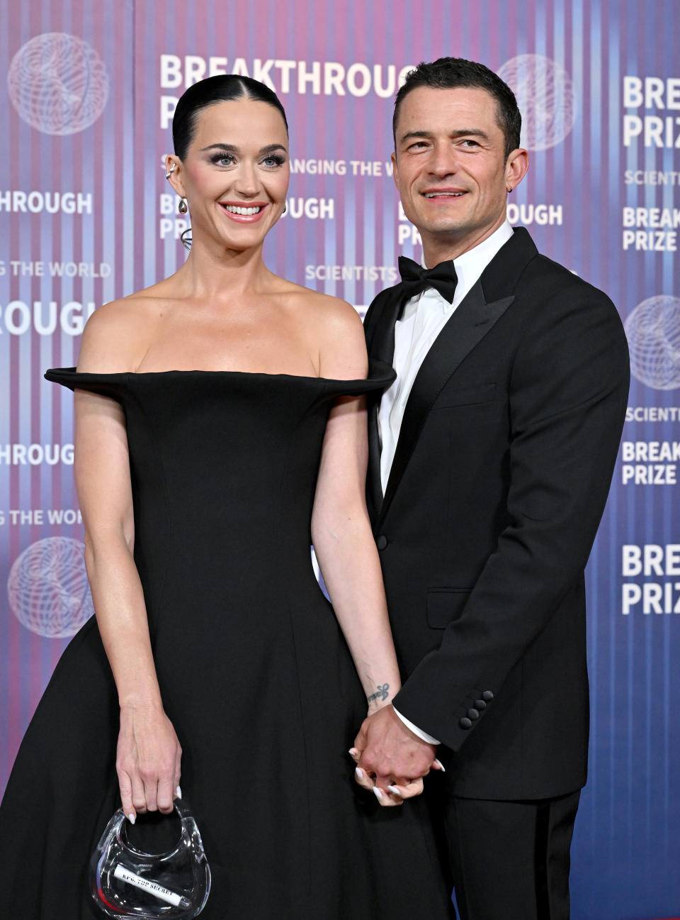 Katy Perry in a strapless dress and Orlando Bloom in a tuxedo hold hands on the red carpet at an event