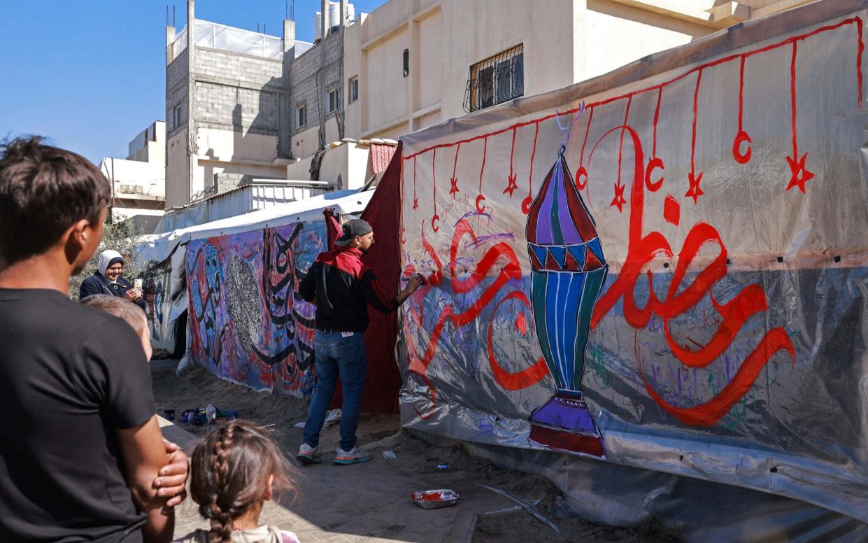 Palestinian artist Ayman al-Husari draws calligraphy on the tent of displaced people along a street in Rafah