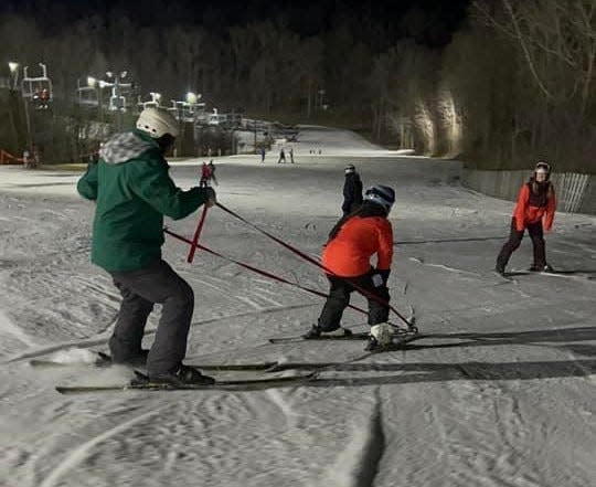 Special Outdoor Leisure Opportunities volunteers use tethers to guide a ski student in winter 2023 at Swiss Valley Ski & Snowboard Area in Jones.
