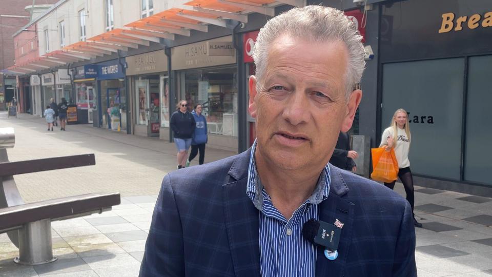 Man with grey hair in suit outside shops