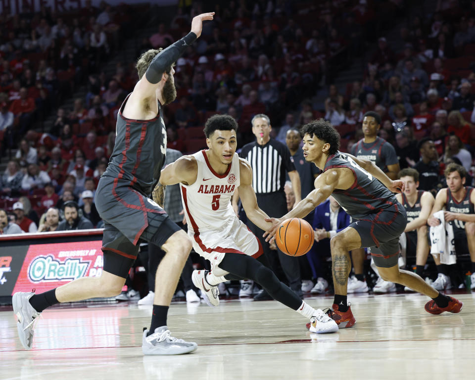 Alabama guard Jahvon Quinerly (5) drives between Oklahoma forward Tanner Groves, left, and guard Milos Uzan, right, during the first half of an NCAA college basketball game Saturday, Jan. 28, 2023, in Norman, Okla. (AP Photo/Garett Fisbeck)