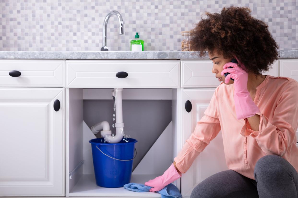 woman on phone with plumber looking at leaky sink