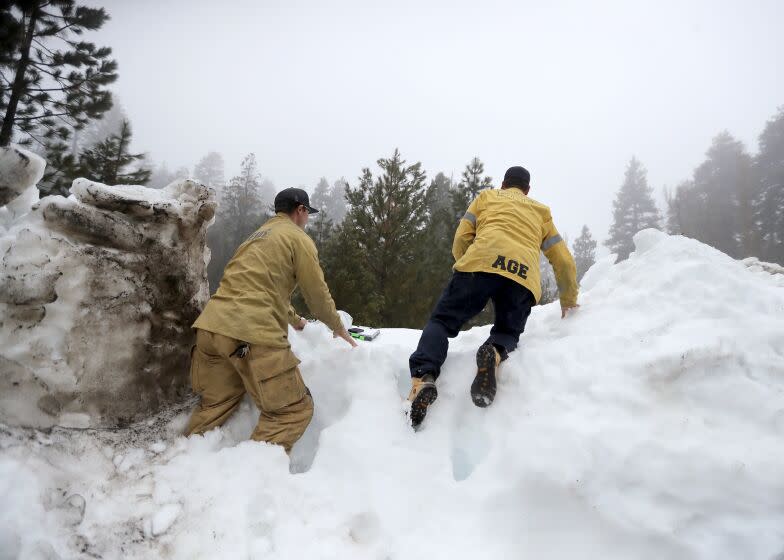 LAKE ARROWHEAD, CA - MARCH 10: Fire line medic Aaron Thomas, left, and medic Mike Age, right, climb a steep snow berm as they attempt to deliver prescription medicine to a snowed-in San Bernardino mountain resident on Friday, March 10, 2023 in Lake Arrowhead, CA. (Brian van der Brug / Los Angeles Times)