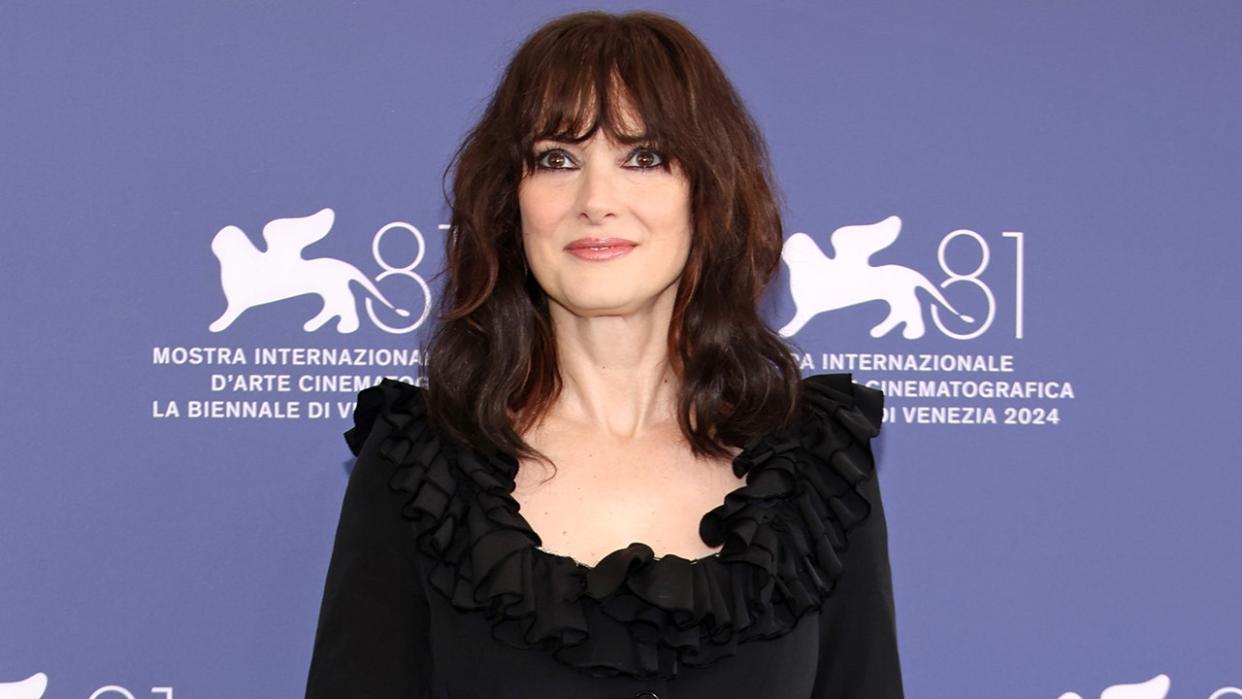 Winona Ryder soft smiles on the carpet in a black dress with ruffles on the top