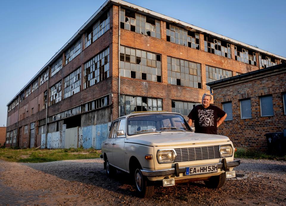 Wolfgang Hofmann stands next to his Wartburg car built in 1974 in front of a wrecked and abandoned production building of the former East German VEB car factory where BMW and Wartburg cars were built in Eisenach, eastern Germany, Tuesday, Sept. 22, 2020. The factory was closed in 1991. Thirty years after Germany was reunited on Oct. 3, 1990, many once-decrepit city centers in the formerly communist east have been painstakingly restored and new factories have sprung up. But many companies and facilities didn't survive the abrupt transition to capitalism inefficient companies found themselves struggling to compete in a market economy, while demand for eastern products slumped and outdated facilities were shut down. (AP Photo/Michael Probst)