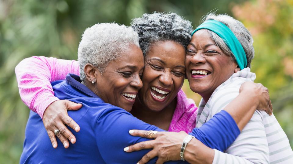 Three senior African American women at the park, hugging.