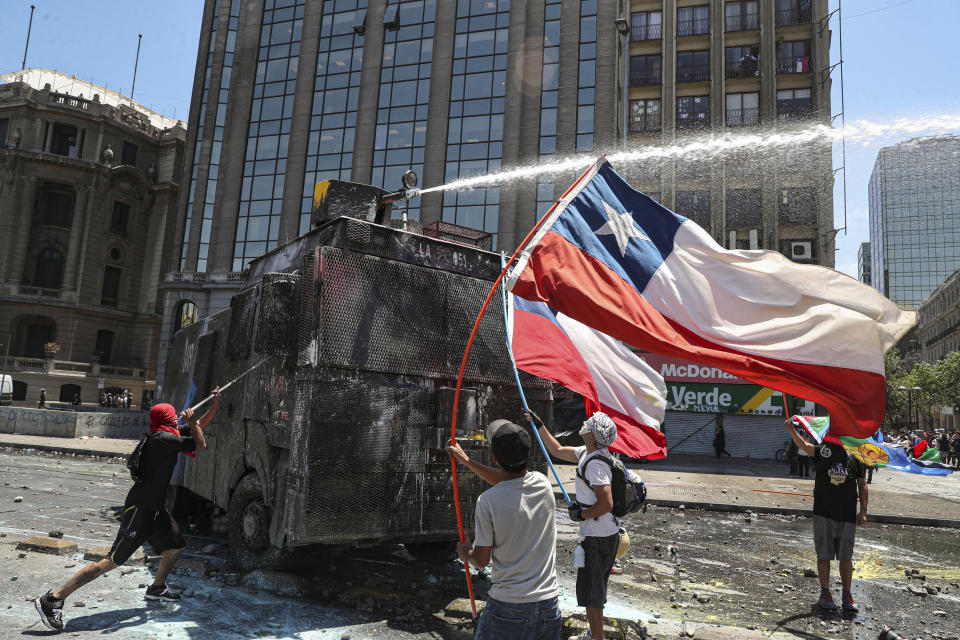 Manifestantes antigubernamentales se enfrentan a un cañón de agua de la policía cerca del palacio presidencial de La Moneda en Santiago, Chile, el martes 12 de noviembre de 2019. (AP Foto / Esteban Felix)