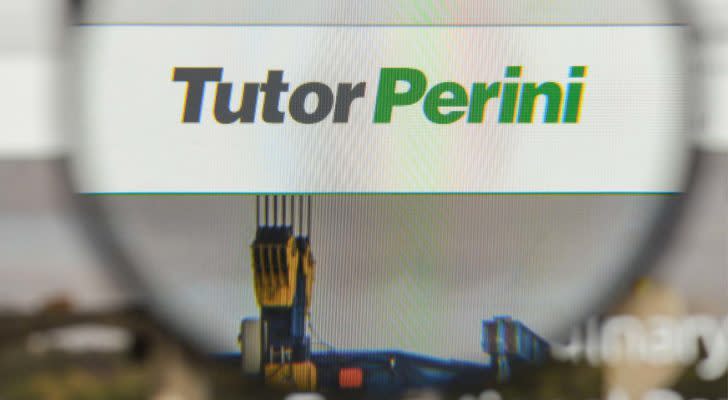 An image of a blurry magnifying glass lens focusing on a screen displaying a white box with a grey top outline and a green bottom outline with the text "Tutor Perini" in a grey and green font.