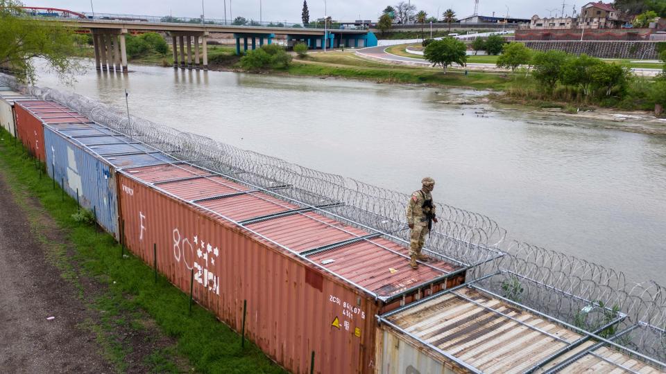 In an aerial view, a Texas National Guard soldier stands atop a barrier of shipping containers and razor wire while guarding the U.S.-Mexico border in Eagle Pass, Texas.