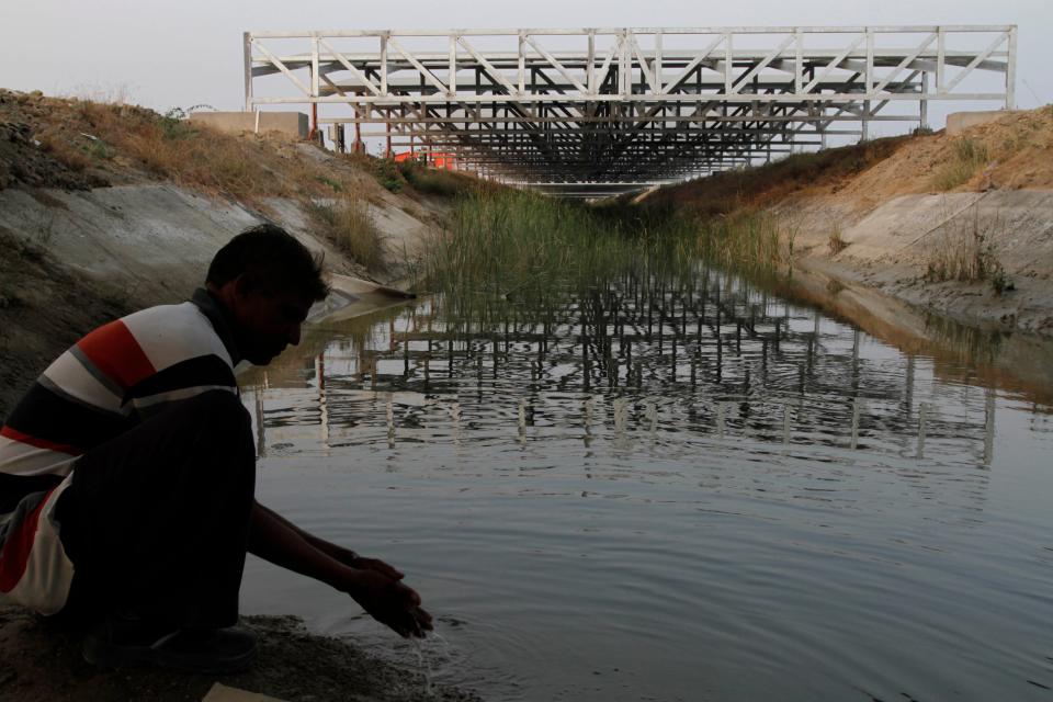 A worker washes his hands as installed solar panels are visible atop the Narmada canal at Chandrasan village, outside of Ahmadabad, India, on Feb. 16, 2012.