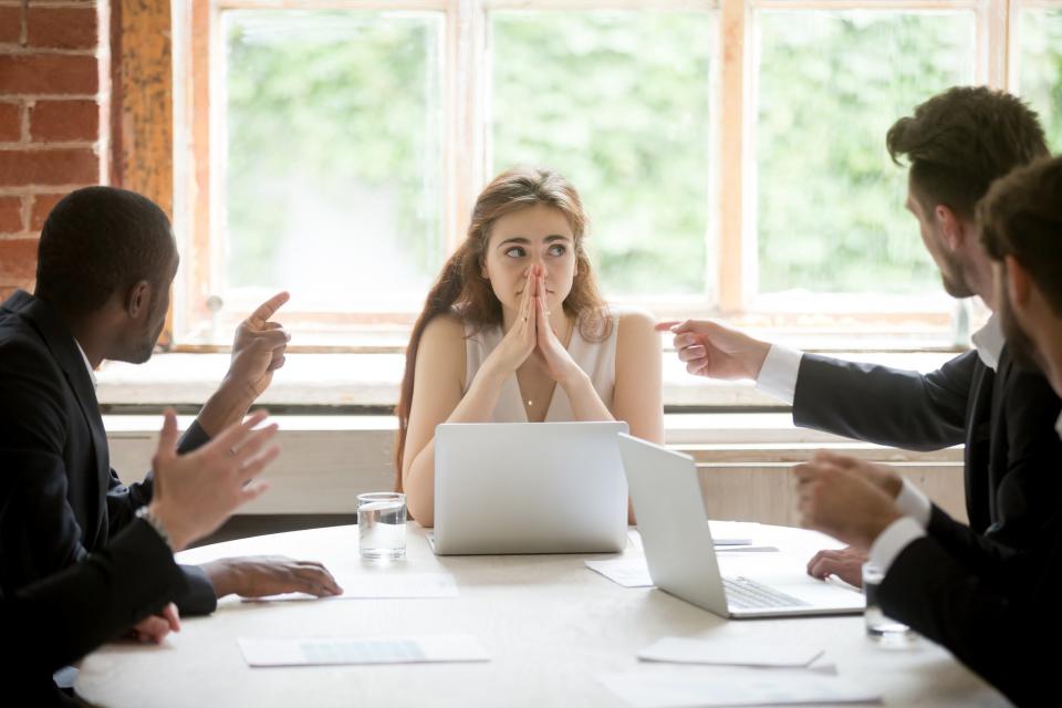 Una mujer siendo cuestionada por sus colegas hombres en el trabajo.