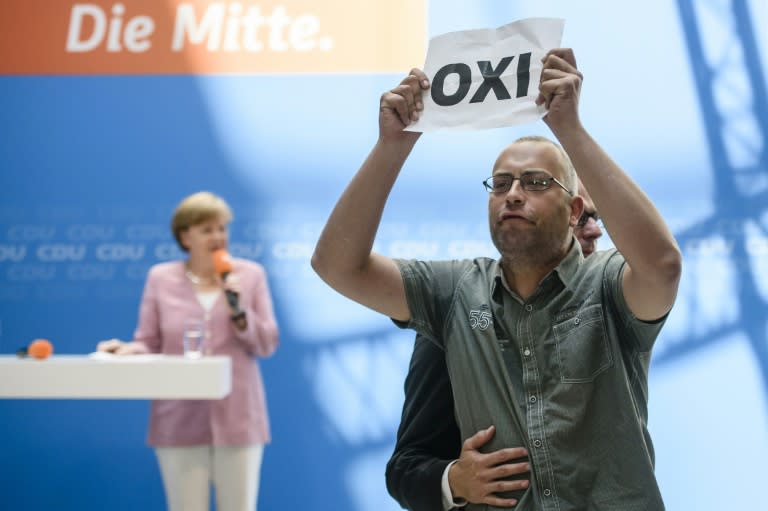 A protester holds a sign bearing the Greek word for 'No' as German Chancellor Angela Merkel speaks during a presentation by Germany's conservative Christian Democratic Union (CDU) party in Berlin, on July 4, 2015